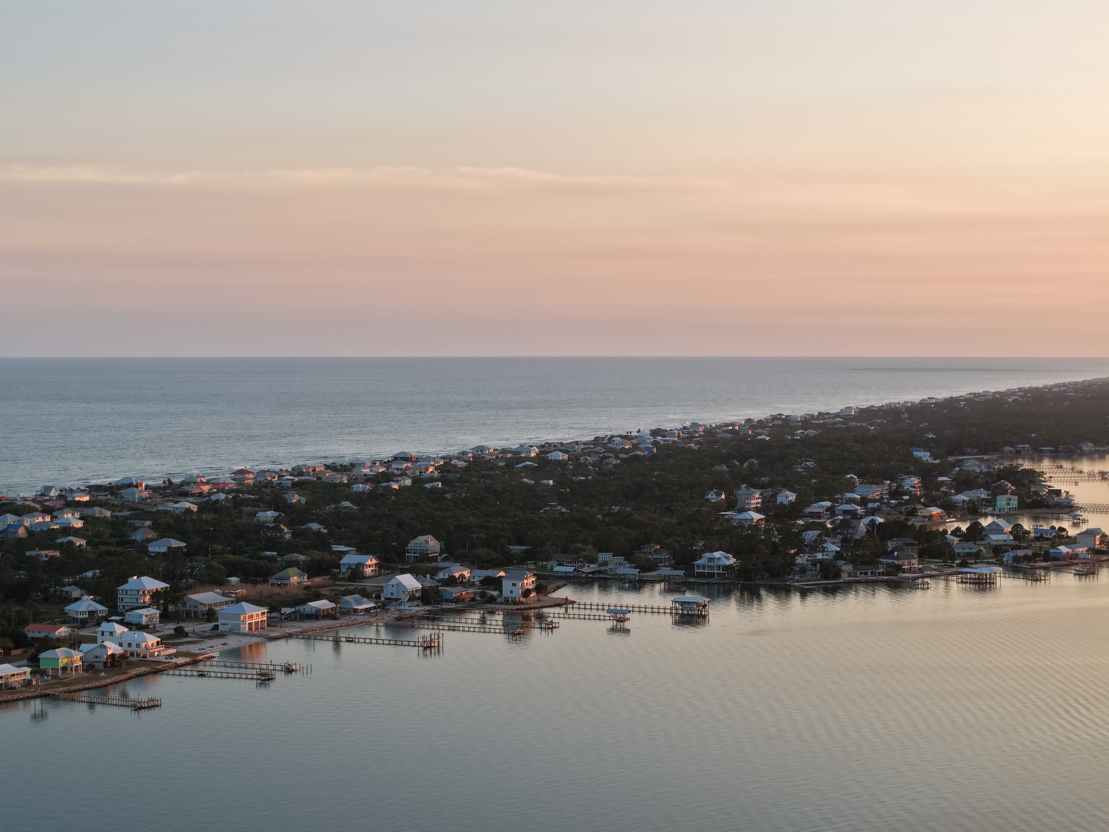 Sunset aerial view of coastal homes between open water and the shoreline